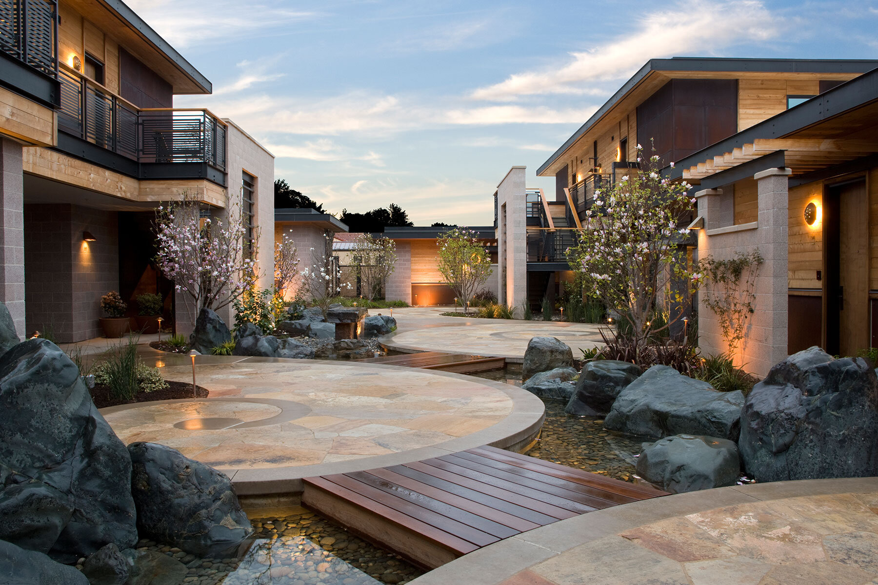 A modern hotel exterior with a courtyard, water feature, and landscaping.