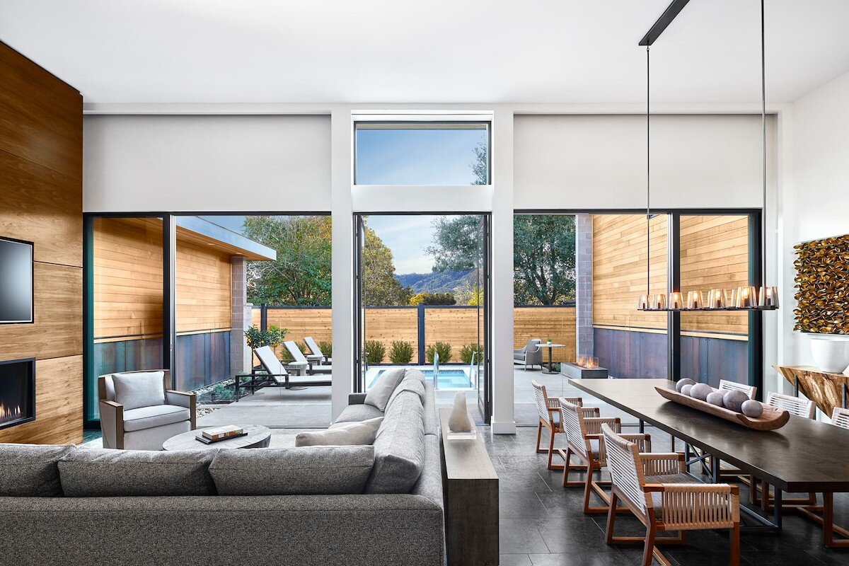 A modern living room with a large window, a fireplace, and a pool in the background.
