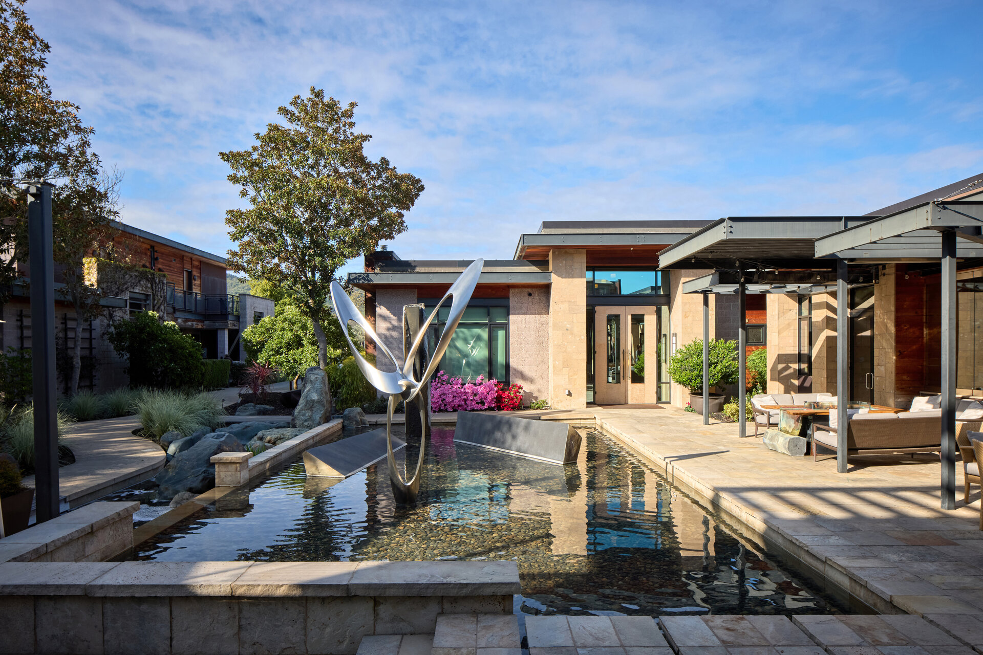 A serene outdoor space with a water feature, modern sculpture, and comfortable seating area.